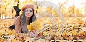Happy smiling young woman in park on a sunny autumn day. Cheerful student girl in sweater with yellow leaves outdoors on