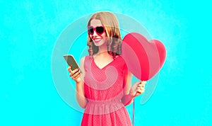 Happy smiling young woman with phone, pink heart shaped air balloons on colorful blue