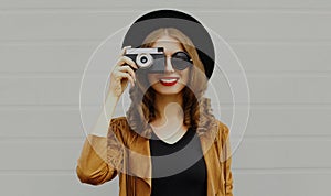 Happy smiling young woman photographer with vintage film camera wearing a boho style on a gray background