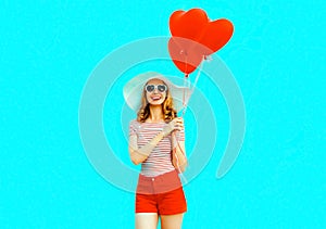 Happy smiling young woman with red heart shaped air balloons in summer straw hat and shorts on colorful