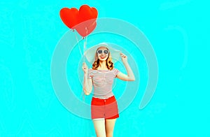 Happy smiling young woman with red heart shaped air balloons in summer straw hat and shorts on colorful