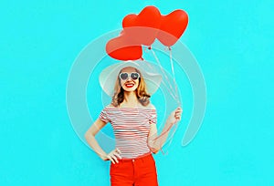 Happy smiling young woman with red heart shaped air balloons in summer straw hat and shorts on colorful blue