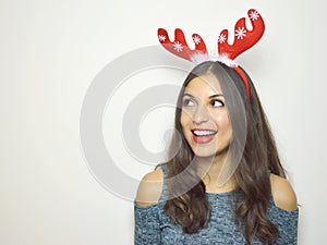 Happy smiling young woman with reindeer horns on her head looks your product on white background. Copy space.