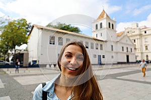 Happy smiling young woman in Sao Paulo city center with Patio do Colegio landmark on the background, Sao Paulo, Brazil