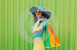 Happy smiling young woman with shopping bags wearing summer straw hat on green background