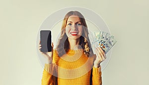 Happy smiling young woman showing black blank screen phone holding cash money in dollar bills