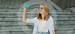 Happy smiling young woman taking selfie picture by smartphone sitting on the stairs