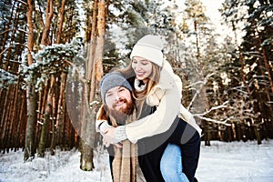 Happy smilling couple. Man giving woman piggyback ride on winter vacation in snowy forest