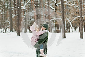 Happy and smilling young mother and her little daughter spending time together, outside in winter forest