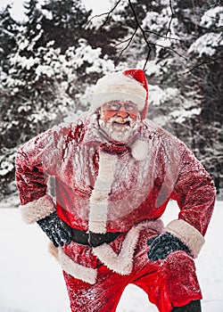 Happy snow-covered Santa Clausthe standing in the snowy winter forst and looks at camera