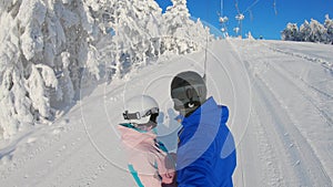 Happy snowboarders couple going up with an anchor ski lift in ski resort. They are enjoying sunny day. Winter vacation