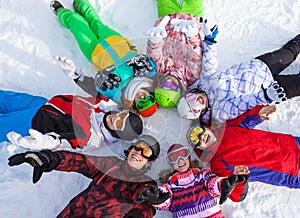 Happy snowboarders lying in circle lifting hands