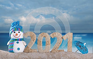 Happy snowman and the inscription 2021 in the sand by the sea