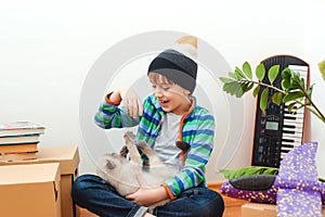 Happy son and a cat having fun together at moving day in new home. Family moves into a new apartment