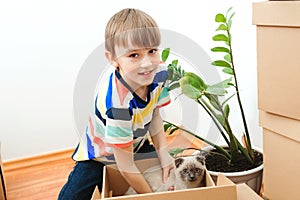 Happy son and a cat having fun together at moving day in new home. Housing a young family with kid and pet