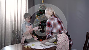 Happy son helping mother kneading dough at home on New Year's eve. Cheerful relaxed Caucasian boy and woman having fun