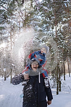 Happy son on shoulders of his father shaking off snow from branch, enjoying winter season