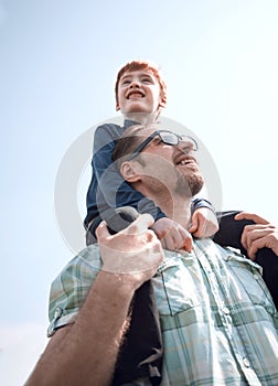 Happy son sits on his father`s shoulders