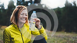 Happy sport girl laughing quenches thirst after fitness. Smile person drinking water from plastic bottles relax after exercising