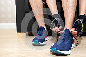 Happy sport man tie shoelace of his running shoe on sofa in home living room for running, jogging, and exercise in fitroom and