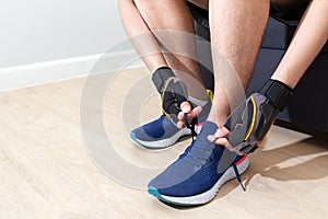 Happy sport man tie shoelace of his running shoe on sofa in home living room for running, jogging, and exercise in fitroom and