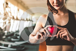 Happy sport woman holding red heart in fitness gym club. Medical cadio heart strength training lifestyle. Pretty female sport girl