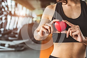 Happy sport woman holding red heart in fitness gym club. Medical cardio heart strength training lifestyle. Pretty female sport