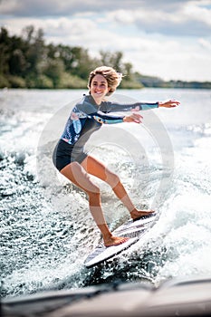 Happy sportive woman riding surf board on the wave from motor boat