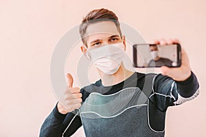 Happy sports man in face mask showing thumb up to phone camera
