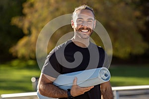 Happy sportsman poses confidently in activewear, holding gym mat outside