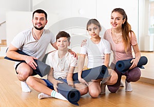 Happy sporty family posing in gym with yoga mats