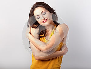 Happy sporty woman hugging herself with natural emotional enjoying face in yellow t-shirt on blue background. Love concept