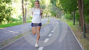 Happy sporty woman jogger doing stretching exercise on road in park