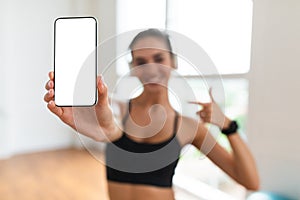 Happy sporty woman pointing at phone with blank screen