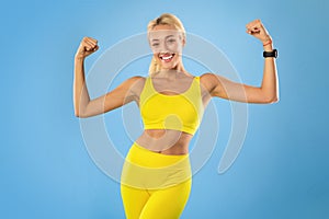 Happy sporty woman showing strong biceps muscles at studio