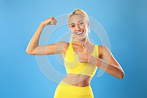 Happy sporty woman showing strong biceps muscles and thumbs up