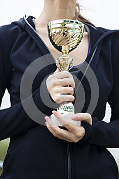 Happy sporty young woman holding gold trophy cup