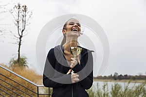 Happy sporty young woman holding gold trophy cup