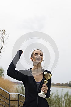 Happy sporty young woman holding gold trophy cup