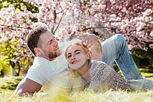 Happy spring couple in love having fun. Two young people relaxing in sakura flowers. Smiling lovers relaxing in park