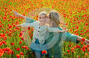 Happy spring family. Carefree mom with a child girl in a field of red poppies enjoys nature. Mother and little daughter