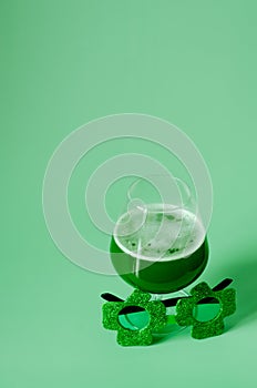 Happy St Patrick`s Day concept. Glass of green beer and party glasses in green background. Greeting card. Top view.