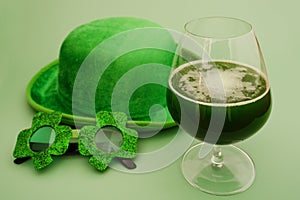 Happy St Patrick`s Day concept. Glass of green beer and party glasses in green background. Greeting card. Top view.