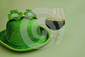 Happy St Patrick`s Day concept. Glass of green beer and party hat in green background. Greeting card. Top view.