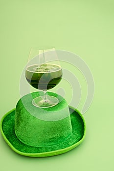 Happy St Patrick`s Day concept. Glass of green beer and party hat in green background. Greeting card. Top view.