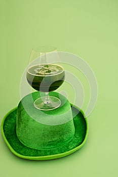 Happy St Patrick`s Day concept. Glass of green beer and party hat in green background. Greeting card. Top view.