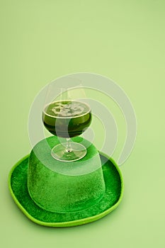 Happy St Patrick`s Day concept. Glass of green beer and party hat in green background. Greeting card. Top view.