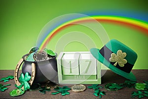 Happy St. Patrick's day. Shiny shamrocks, gold coins and leprechaun hat on a wooden background with rainbow