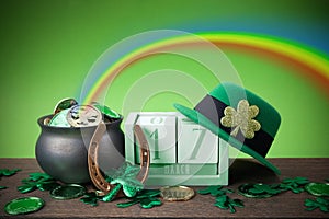 Happy St. Patrick's day. Shiny shamrocks, gold coins and leprechaun hat on a wooden background with rainbow