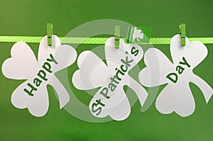 Happy St Patricks Day message greeting written across white shamrocks hanging from pegs on a line